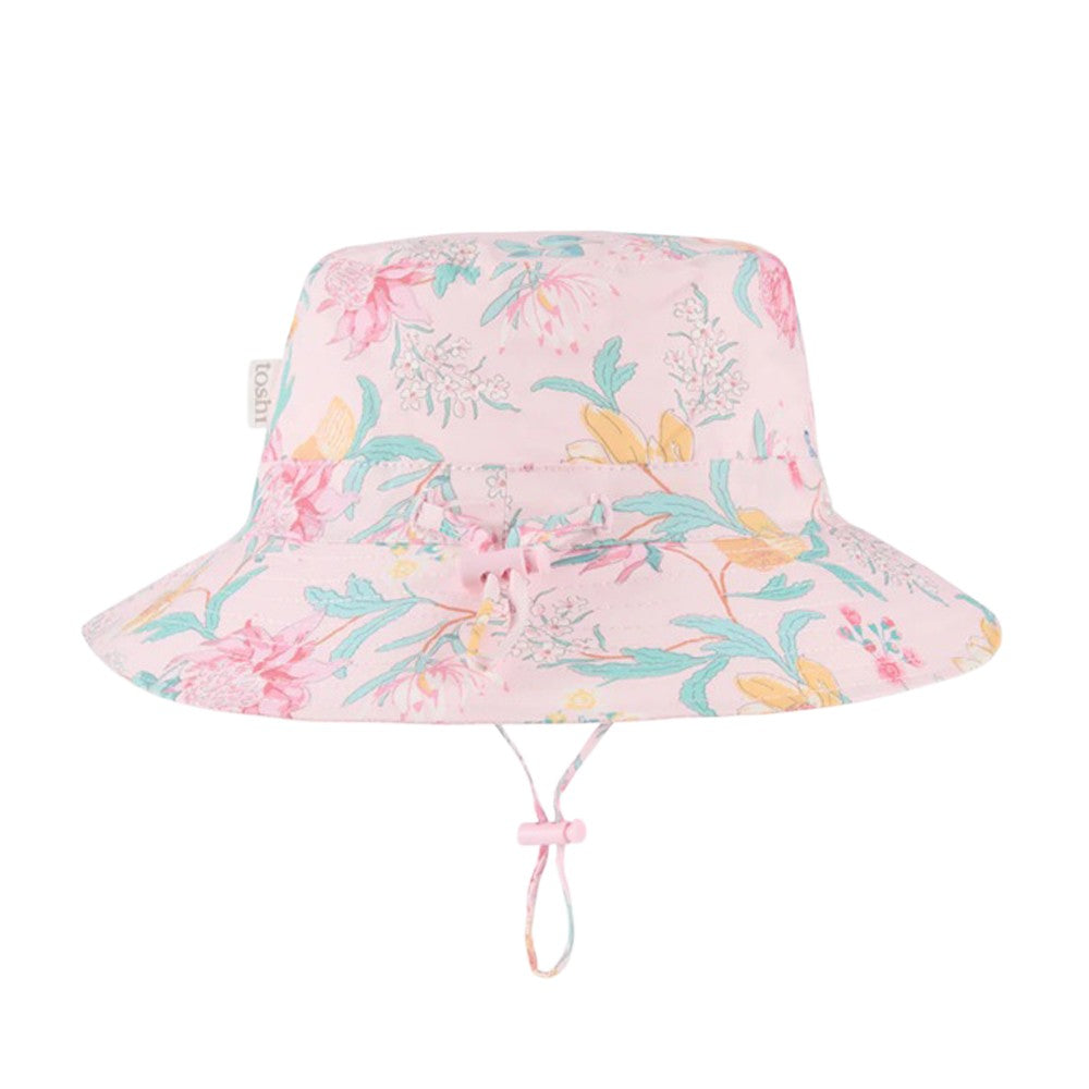 The Toshi Sunhat Waratah Blossom by Toshi is a light pink cotton children’s sunhat with colorful floral prints, green leaves, UPF 50+ protection, and an adjustable chin strap with a pink toggle.