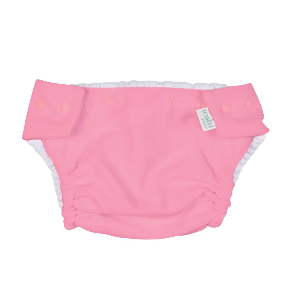 The Toshi Swim Nappy Beachcomber Watermelon is a pink reusable swim nappy with white elastic leg openings, snap side buttons, and a fabric waistband tag—ideal for stylish and practical baby swimwear.