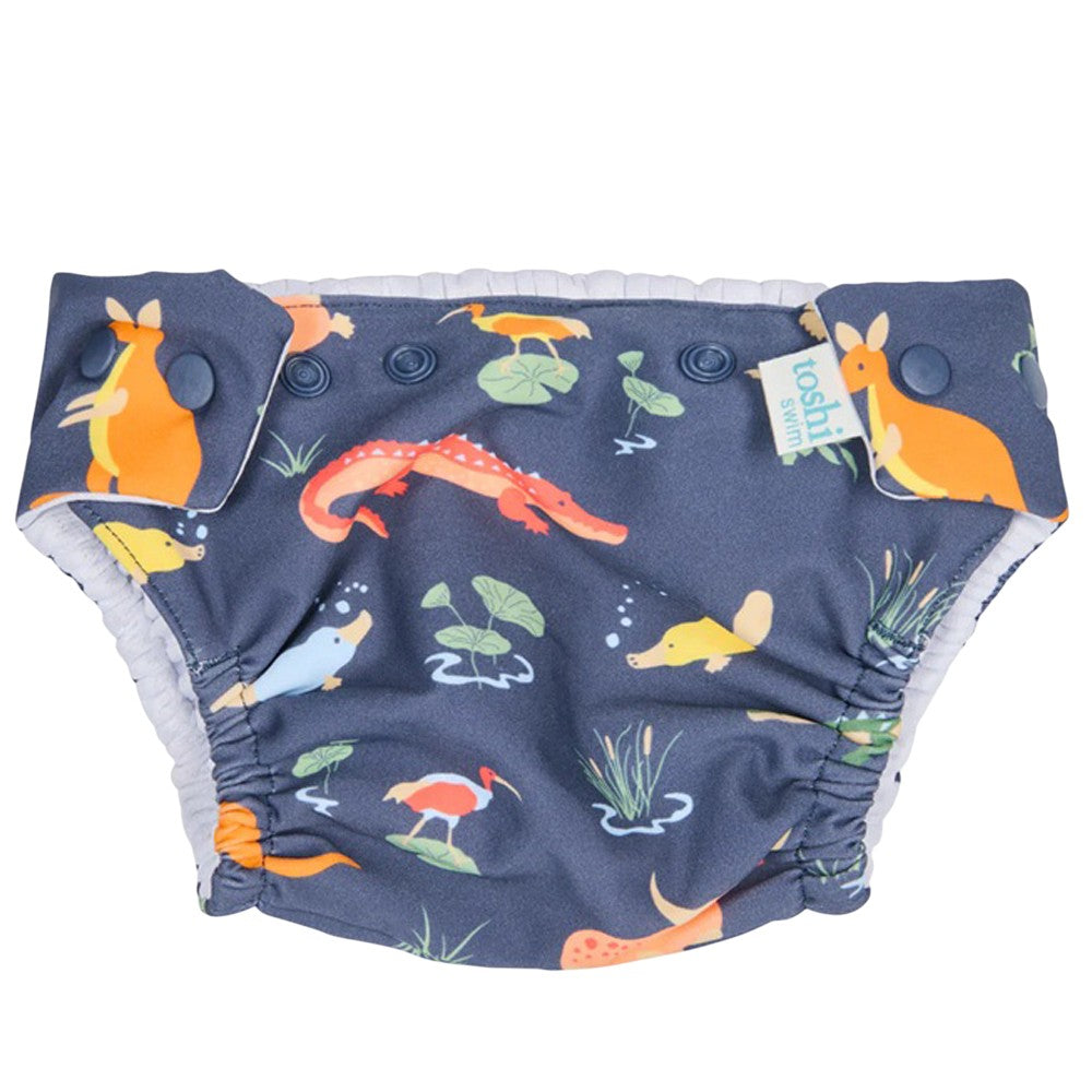 The Toshi Swim Nappy Paradise Kakadu Moonlight features a colorful Australian animal print on dark blue, with kangaroos, crocodiles, platypuses, and birds. It has side snaps, elastic at legs and waist, and provides UPF50+ sun protection for babies.