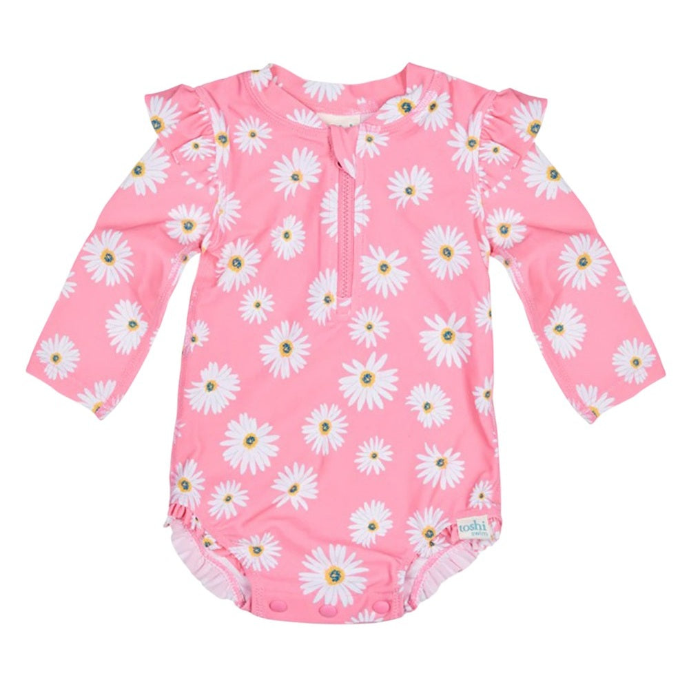 The Toshi Swim Onesie L/S Ripple Daisy Watermelon features long sleeves, pink fabric with white daisy patterns, ruffled shoulders, UPF 50+ protection, and bottom snaps for easy diaper changes.