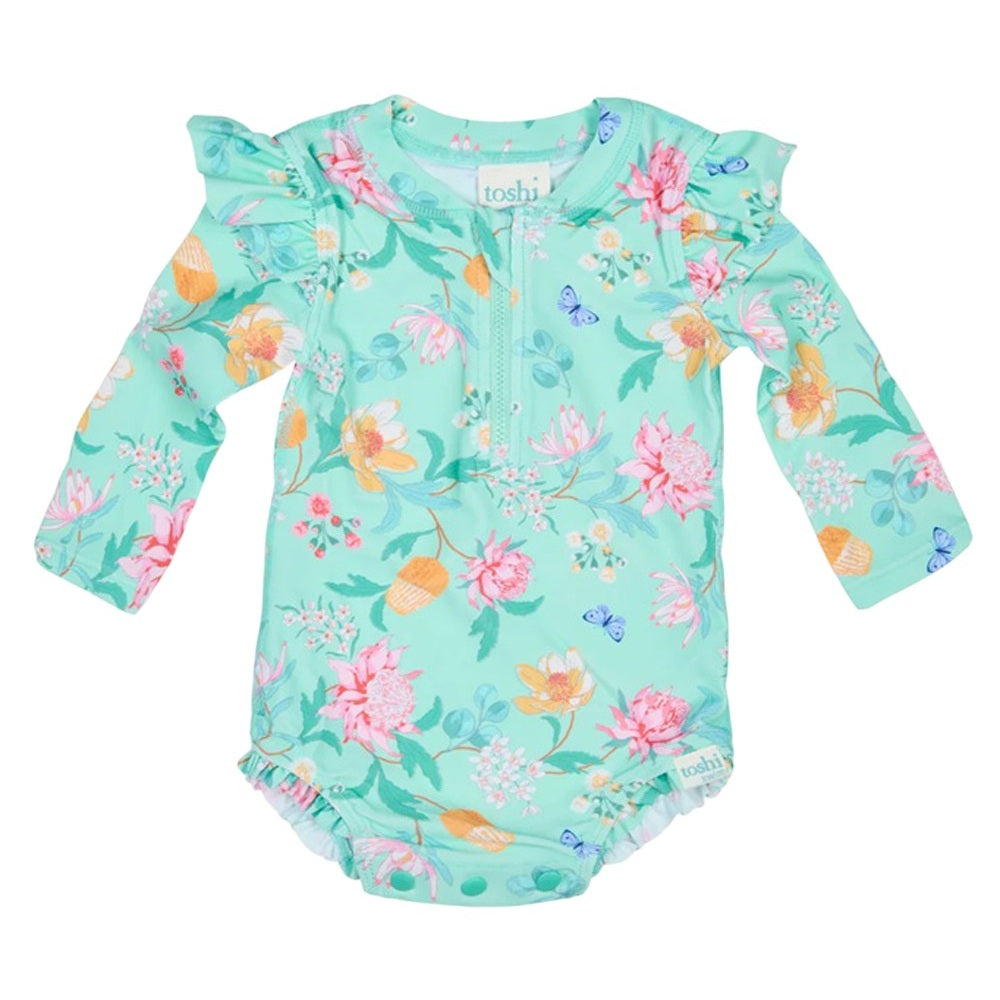 The Toshi Swim Onesie L/S Ripple Waratah Mint is a long-sleeve baby swimwear romper in aqua with colorful florals and butterflies, ruffled shoulders, a front zipper, and UPF 50+ sun protection.