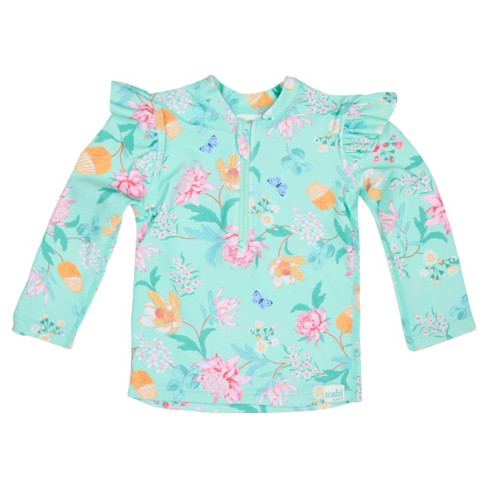 The Toshi Swim Rashie L/S Ripple Waratah Mint is an aqua blue long-sleeve children's rashie with floral and butterfly print, ruffled shoulders, short front zipper, and UPF50+ sun protection from Toshi.