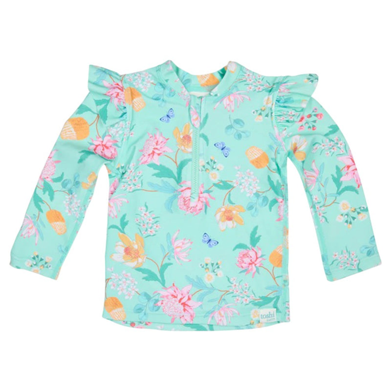 The Toshi Swim Rashie L/S Ripple Waratah Mint is an aqua blue long-sleeve children's rashie with floral and butterfly print, ruffled shoulders, short front zipper, and UPF50+ sun protection from Toshi.