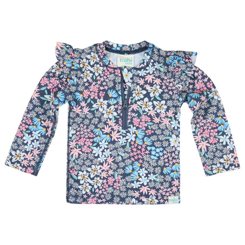 The Toshi Swim Rashie L/S Ripple Wattle Dusk features colorful floral prints, ruffled shoulders, a zippered front, and UPF50+ protection—perfect for stylish children's swimwear.