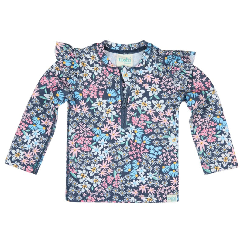 The Toshi Swim Rashie L/S Ripple Wattle Dusk features colorful floral prints, ruffled shoulders, a zippered front, and UPF50+ protection—perfect for stylish children's swimwear.