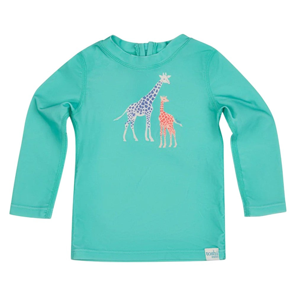 The Toshi Swim Rashie L/S Splash Congo Seagrass by Toshi is a turquoise long-sleeve rashie for kids, featuring two spotted giraffes—one purple, one orange—in the center. It offers UPF50+ sun protection, perfect for outdoor swim fun.