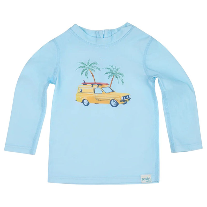 The Toshi Swim Rashie L/S Splash Swell Seekers Sky is a light blue long-sleeve baby rash guard with a yellow station wagon, surfboard, and palm tree print. Featuring UPF50+ protection and a "toshi" label at the hem—ideal for sunny days.
