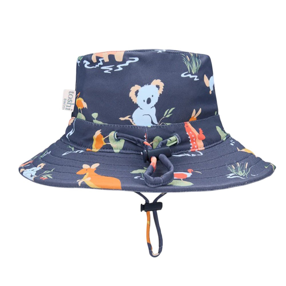 The Toshi Swim Sunhat Paradise Kakadu Moonlight is a navy swim bucket hat with chin strap, featuring colorful animal, plant, and water designs. It offers UPF50+ sun protection and pairs perfectly with your favorite baby swimwear.