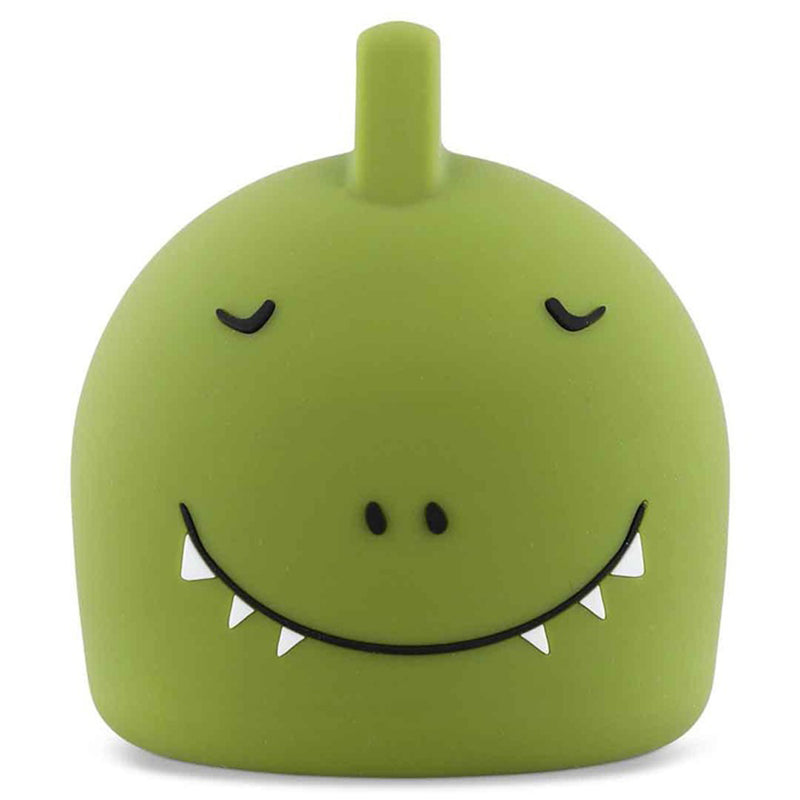 The Trixie Night Light Mr Dino by Trixie is a small, green, rounded toy night light made of soft silicone, featuring a single short top horn, closed eyes, two nostrils, and a wide smile showing three white triangular teeth on each side.