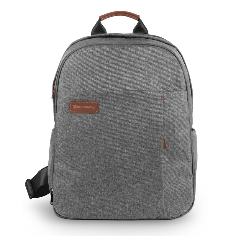 The UPPAbaby Nappy Bag Pro is a gray fabric backpack with brown leather accents, front pocket, top handle, and a leather patch featuring the UPPAbaby logo. This baby changing bag offers a simple, modern design for stylish convenience.