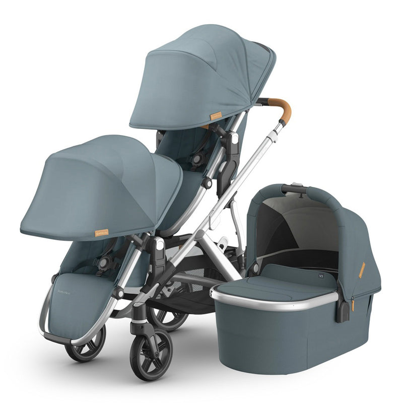 The UPPAbaby Vista V3 Double is a muted blue double stroller with brown accents, a reversible toddler seat, matching bassinet, canopies, metallic silver frame, all-wheel suspension, and black wheels.