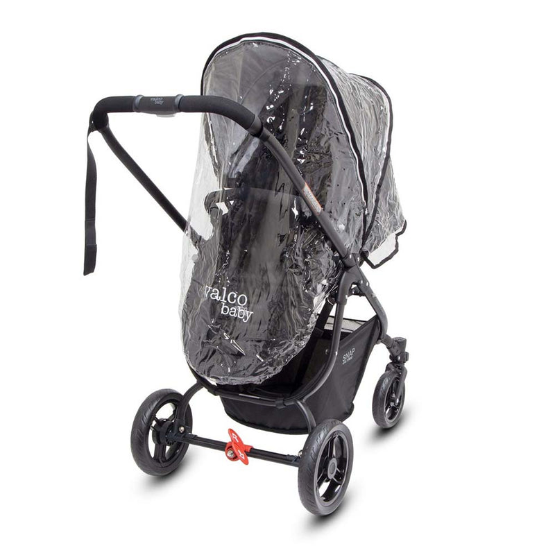 A Valco Baby Snap Ultra/Trend Raincover is shown on a black Valco Baby pram against a white background. The clear cover shields the seat from wind and rain, and there’s a black storage basket under the four-wheeled pram.