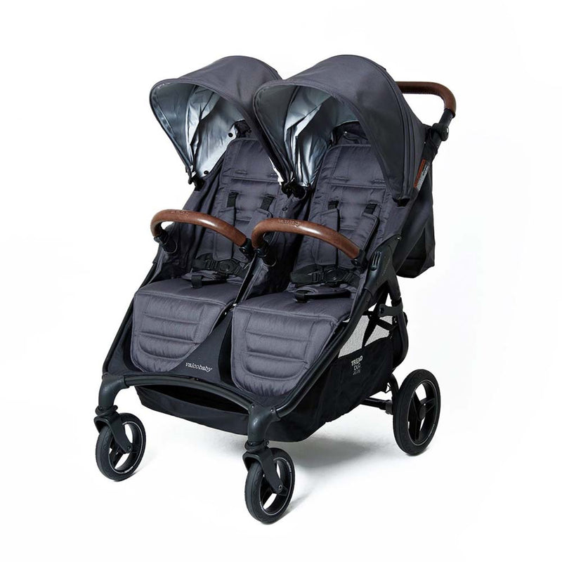 The Valco Baby Trend Duo Elite by Valco Baby is a black, lightweight double pram with side-by-side seats, adjustable canopies, safety harnesses, and brown leatherette handle and bumper bars—ideal as a compact travel pram for two children.