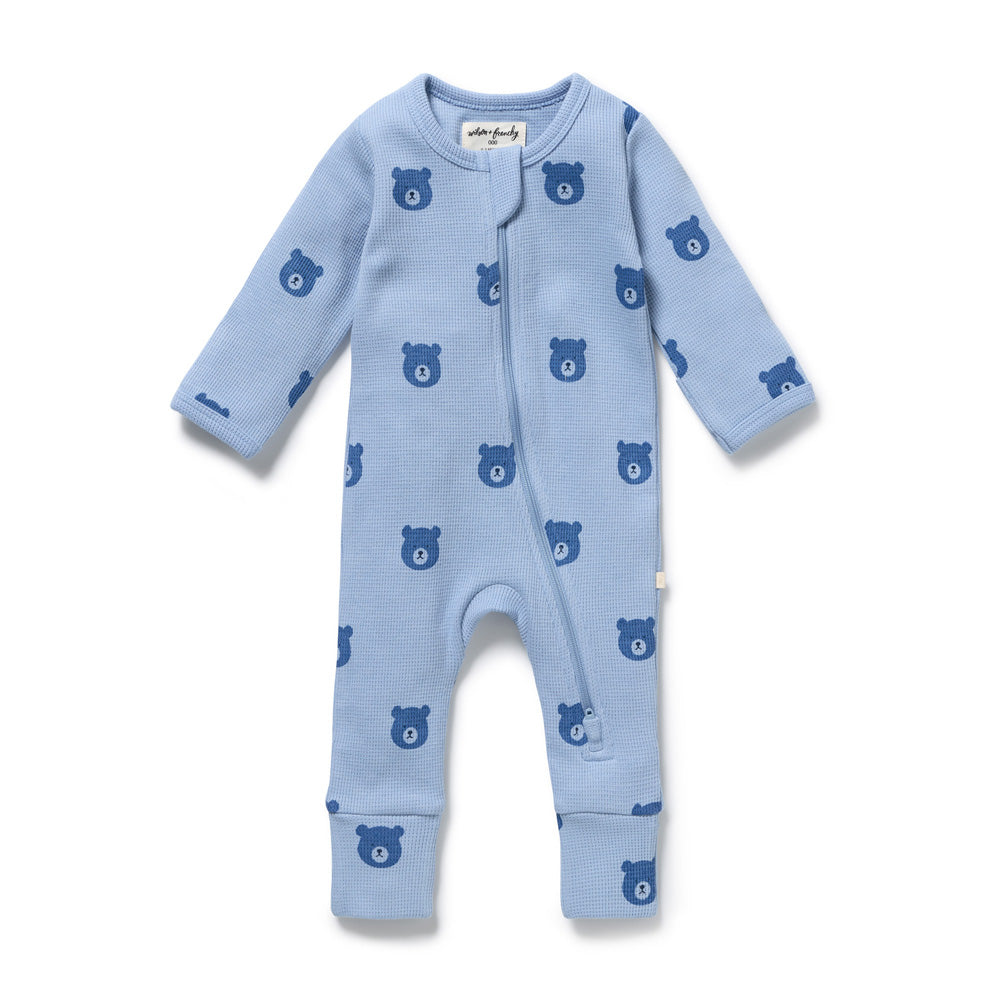 The Wilson & Frenchy Bear Hugs Organic Waffle Zipsuit is a light blue, GOTS-certified baby sleepsuit with long sleeves and legs, darker blue bear face pattern, and a diagonal front zipper from collar to left leg.