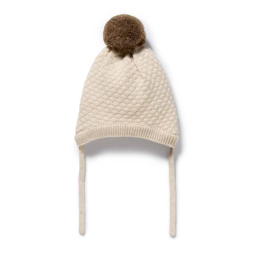 The Wilson & Frenchy Cream Organic Knitted Bubble Bonnet features a textured knit, ear flaps, long ties, and is topped with a large brown pom-pom.