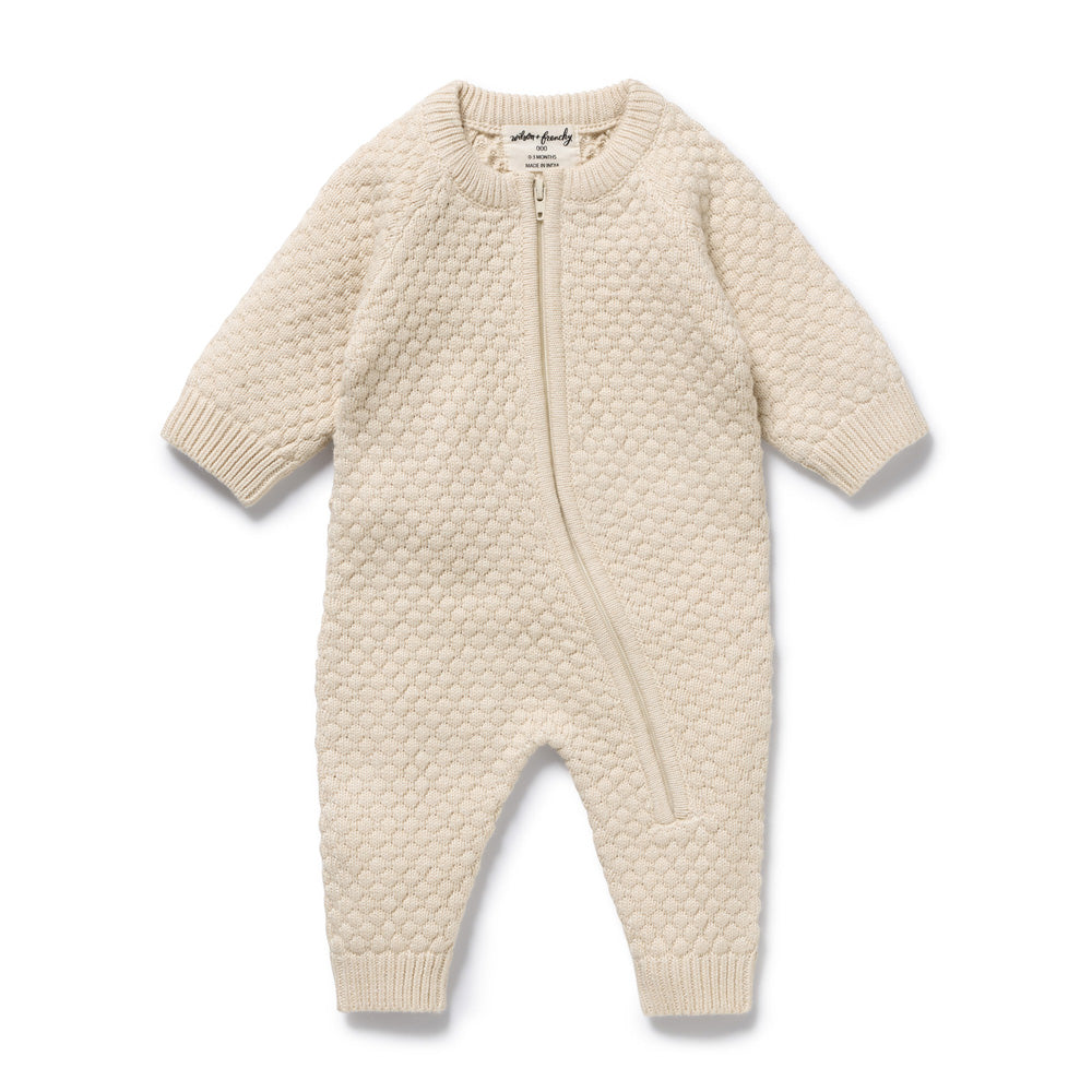 The Wilson & Frenchy Cream Organic Knitted Bubble Growsuit is a textured knit baby onesie with long sleeves and legs, featuring an asymmetrical zipper from the neckline to one leg.