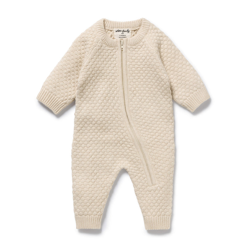The Wilson & Frenchy Cream Organic Knitted Bubble Growsuit is a textured knit baby onesie with long sleeves and legs, featuring an asymmetrical zipper from the neckline to one leg.