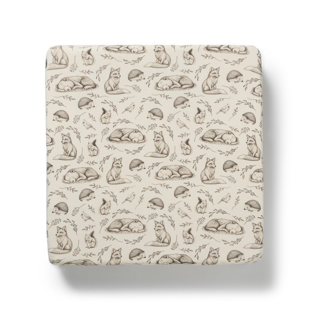 The Wilson & Frenchy Foxglove Forest Organic Sheet is a cream-colored fitted sheet featuring brown-toned sketched foxes, hedgehogs, and plants, shown from above on a white background.