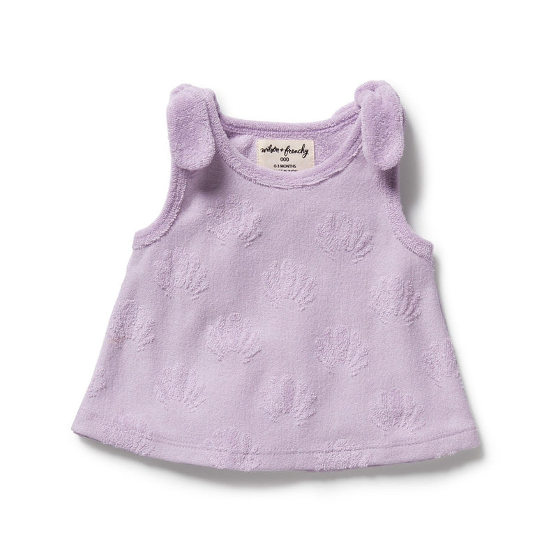 The Wilson & Frenchy Lavender Shells Organic Terry Singlet is a sleeveless, GOTS-certified organic cotton baby dress with floral textures and soft shoulder bows—ideal for kids’ summer wear, shown on a white background.