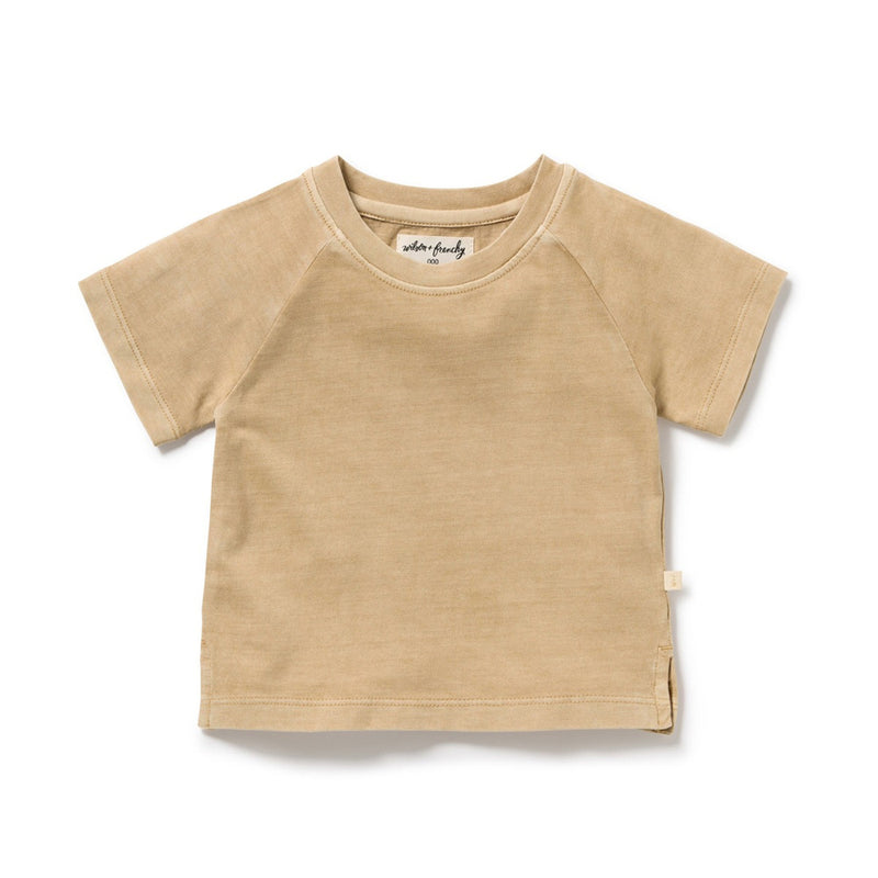 The Wilson & Frenchy Sahara Organic Dyed Tee is a beige toddler t-shirt made from soft organic cotton, featuring short sleeves, a round neckline, simple stitching, and a small fabric tag on the side hem.