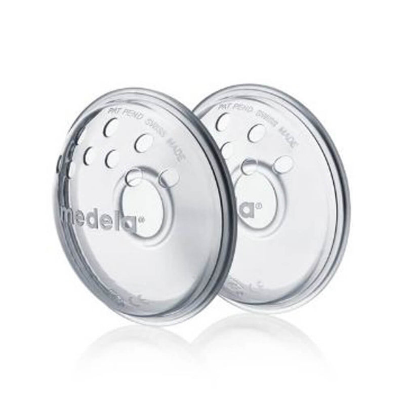 Two clear, round Medela Nipple Formers with the "medela" logo and multiple ventilation holes stand upright and slightly overlap on a white background. Designed for inverted nipples.