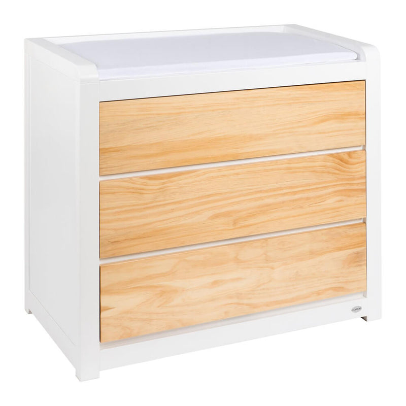 The Cocoon Luxe Change Table by Cocoon features a white and light wood design, three drawers, and a cushioned top—offering stylish storage and comfort for any nursery.