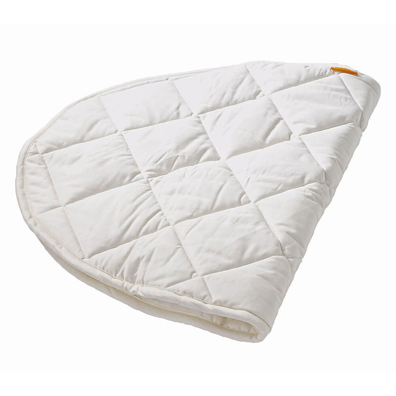 The Leander Classic Organic Mattress Protector by Leander is a white, quilted, semi-circular cover with a grid pattern, partially folded to fit the Leander Classic Cot, shown against a plain white background.