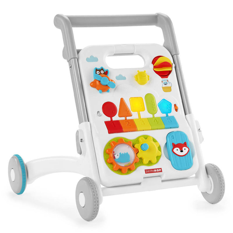The Skip Hop Explore & More Grow Along 4-in-1 Activity Walker is a colorful baby learning toy with four wheels, a white activity panel featuring animals, shapes, spinning gears, a hot air balloon, numbered tiles, and blue-accented gray and white frame.