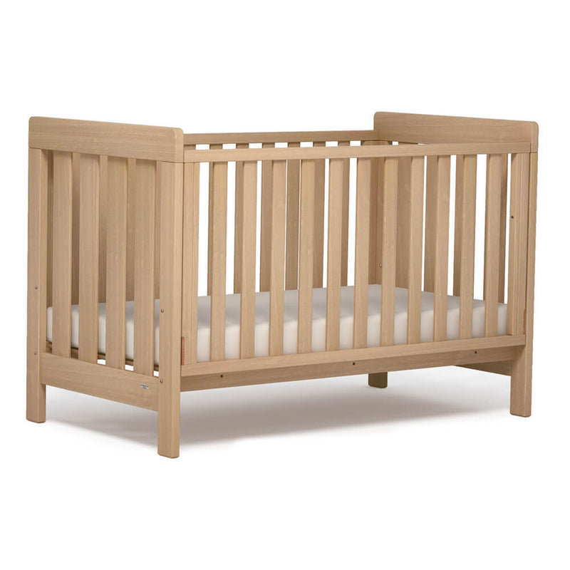 The Boori Daintree Cot by Boori features solid Australian Araucaria, vertical slats on all sides, a safe track drop side system, and a white mattress, shown against a plain white background.