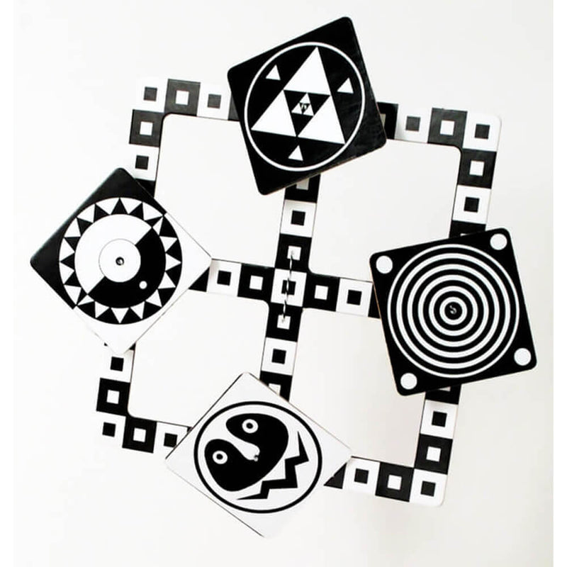 The Tina Matthews Black & White Mobile by Tina Matthews features four black-and-white cards with geometric patterns—concentric circles, triangles, zigzags, and a face—on a grid to visually stimulate your baby’s development.