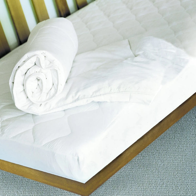 A neatly rolled white comforter sits on a white mattress topped with the Living Textiles Smart-dri Mattress Protector by Living Textiles, set on a wooden bed frame against a carpeted floor.
